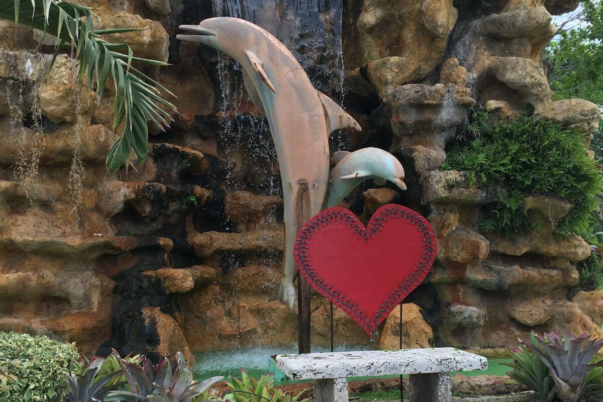 Statues of two dolphins and a heart in front of a waterfall. 