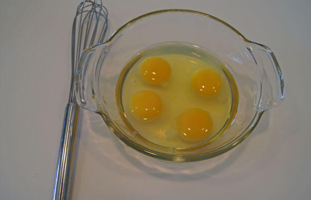 four eggs in a bowl next to a whisk