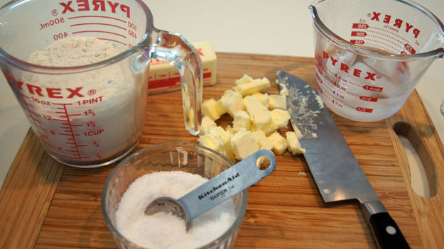 Diced butter next to cups of sugar and flour. 