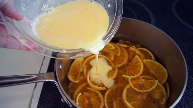 Cream mix being poured over oranges in a pot