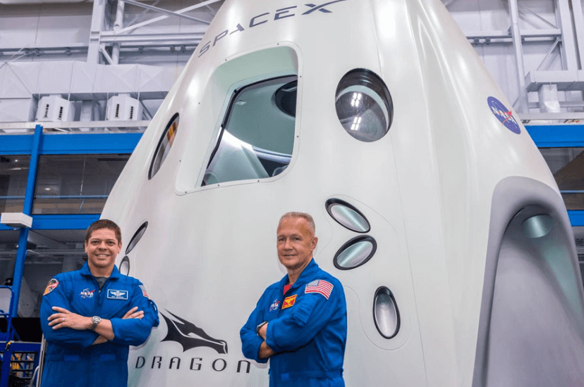 Two astronauts stand in front of a rocket