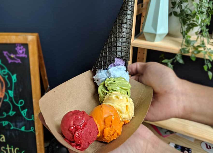 Black cone with ice cream in rainbow colors spilling into a bowl