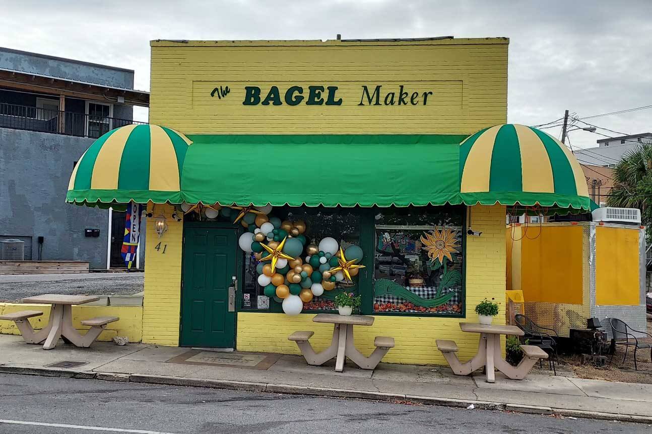 Exterior of a green and yellow shop with the words The Bagel Maker on the front of it. 
