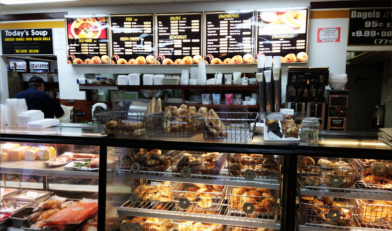 Interior of restaurant showing a display cased filled with bagels and with menus on the wall. 