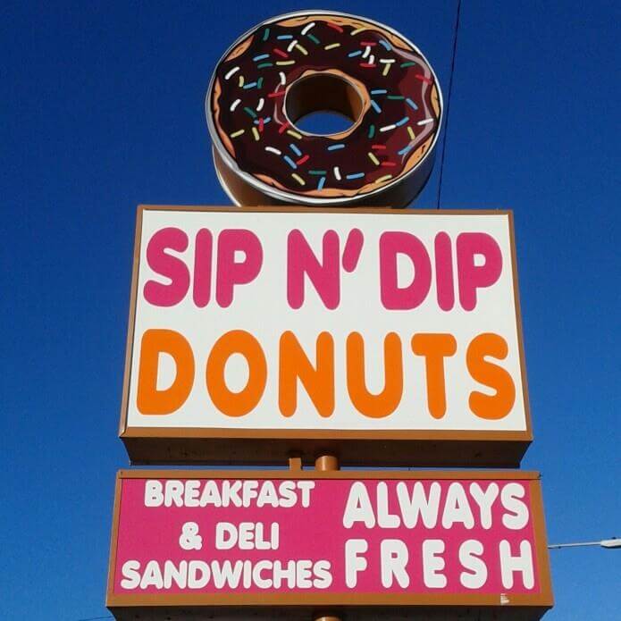 Signs that read Sip N' Dip Donuts Breakfast & Deli Sandwiches Always Fresh. 