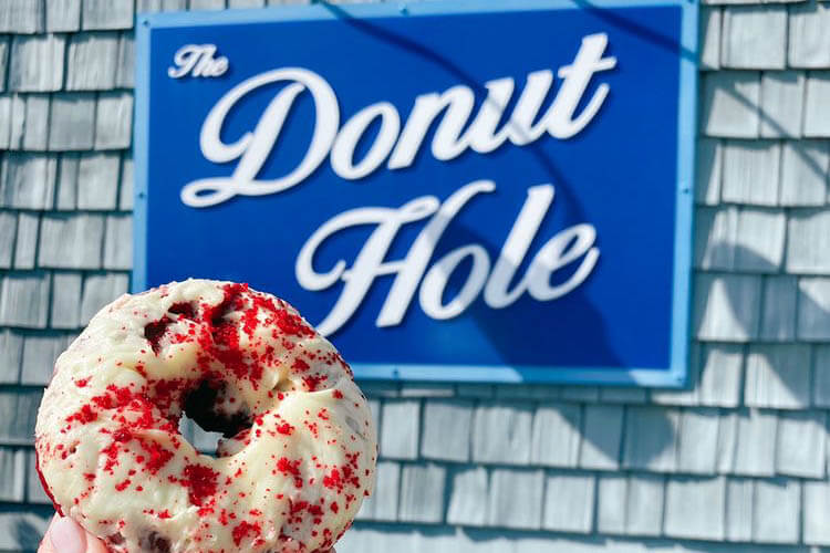 Donut in front of a sign that reads The Donut Hole. 