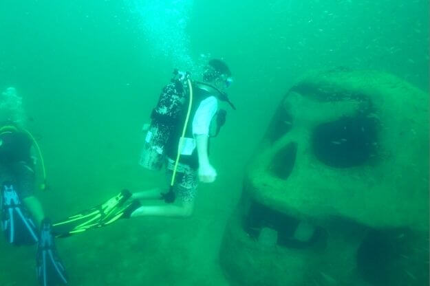 Scuba diver near a skull sculpture.