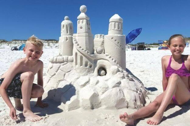 Children on the beach next to a sand castle.