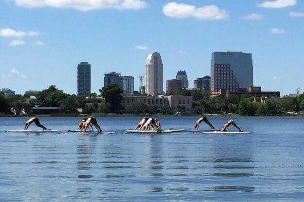 People practicing yoga on lake.