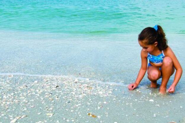 girl crouching to pick up shells at one of Southwest Florida's Best Shell Destinations.