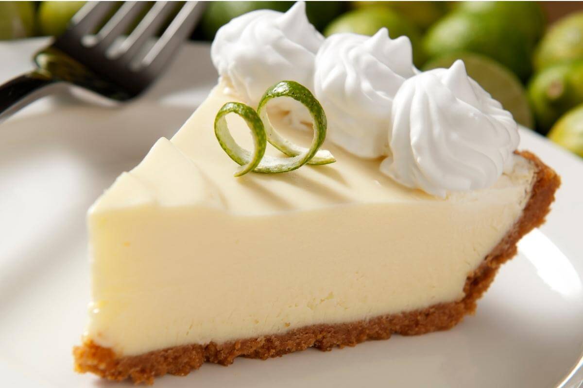 Slice of key lime pie with a curly lime peel. 