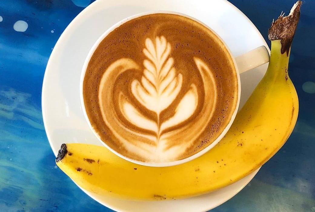 Coffee in a mug with latte art on the top and a banana next to it. 