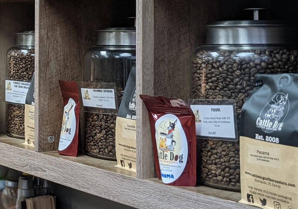 Jars of coffee beans. Bags of coffee beans are in front of the jars and are labeled Cattle Dog Coffee Roasters. 