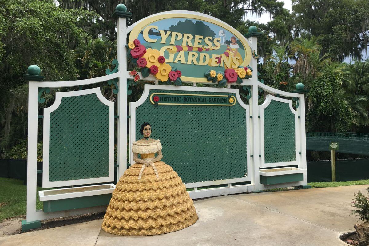 Sign reading Cypress Gardens with a lego statue of a woman in a yellow dress. 