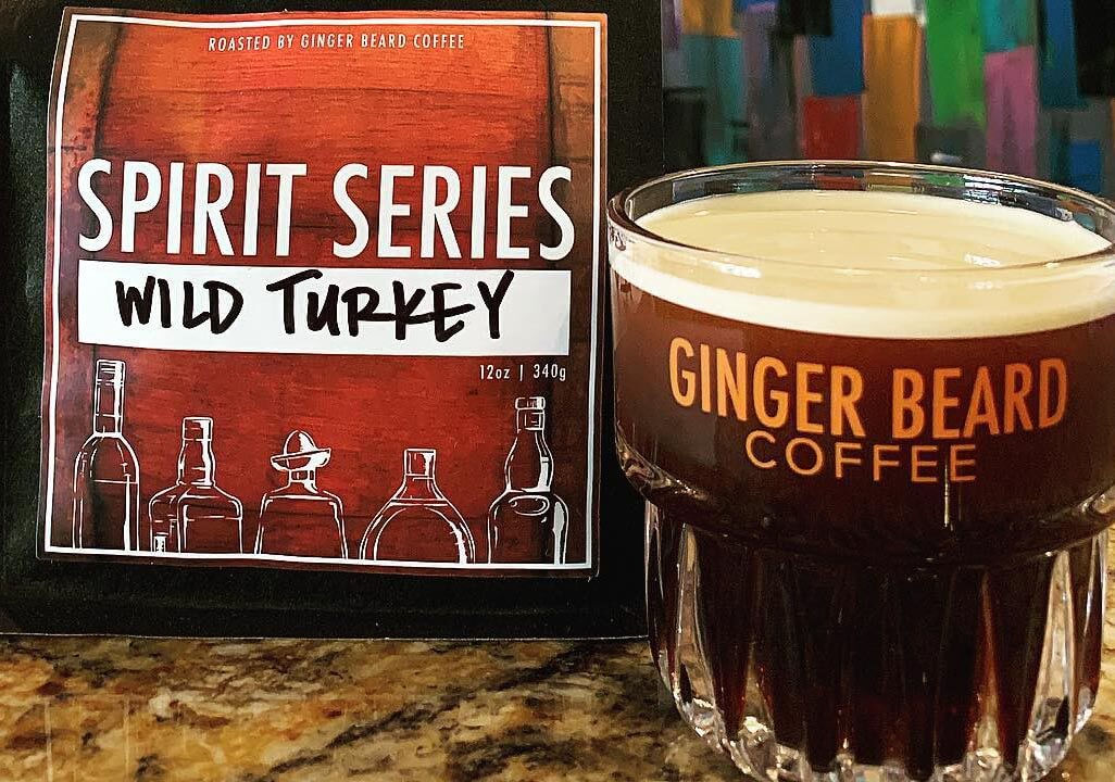 Glass of coffee and bag of coffee. Coffee bag says Spirit Series Wild Turkey and glass says Ginger Beard Coffee. 