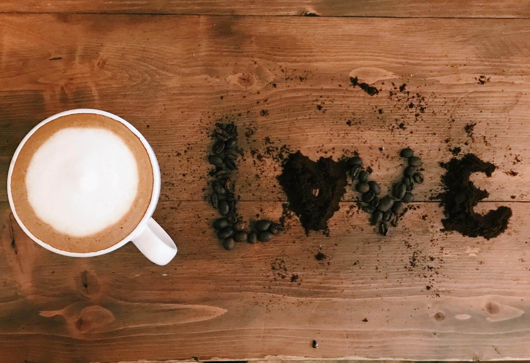 Aerial picture of a glass of coffee and the word Love spelled in coffee beans. 