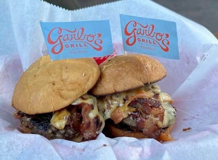 Cheeseburgers in a plate with flags on top that read Garbo's Grill. 