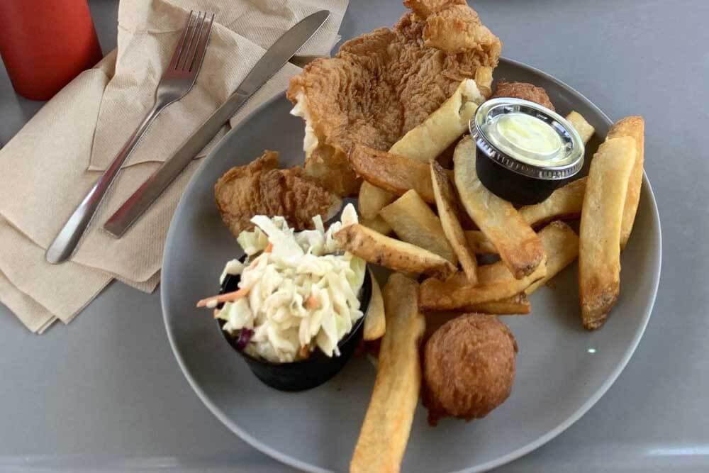 Fish, fries, and corn fritters on a place with cole slaw. 