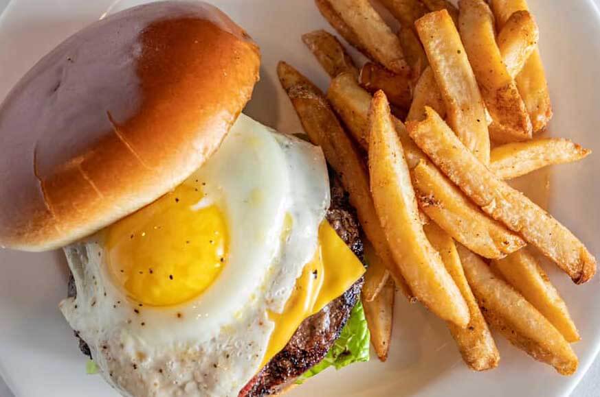 Cheeseburger with a fried egg on top and fries on the side. Served at Historia Pub Burger in Florida 