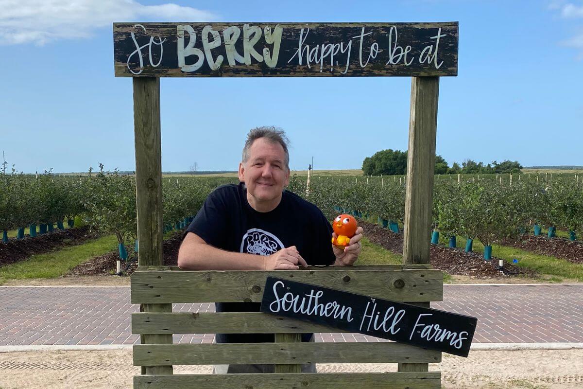 Man holding orange bird in front of a sign for Southern HIll Farms. 