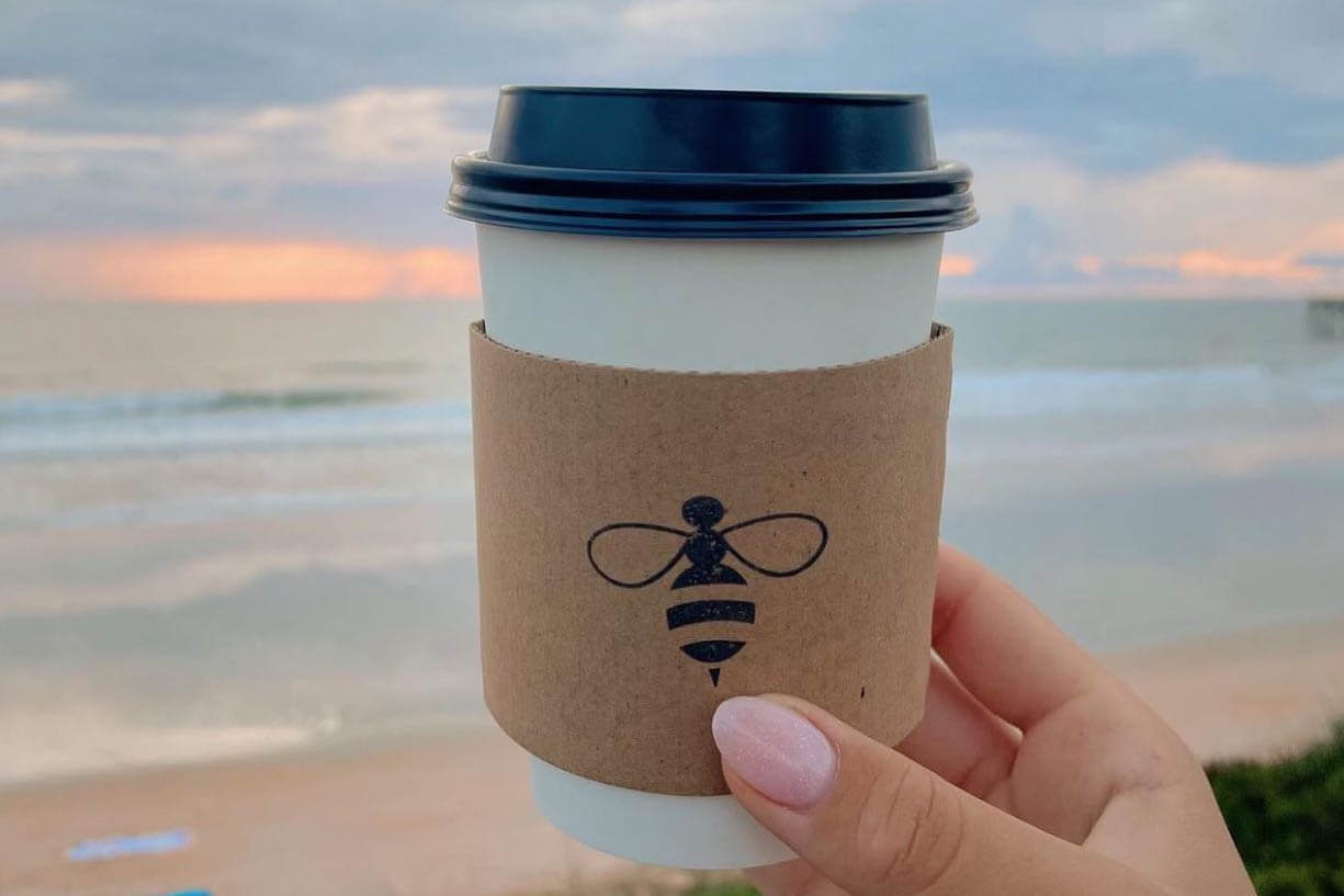 Coffee at the beach with a bee on the heat sleeve. 