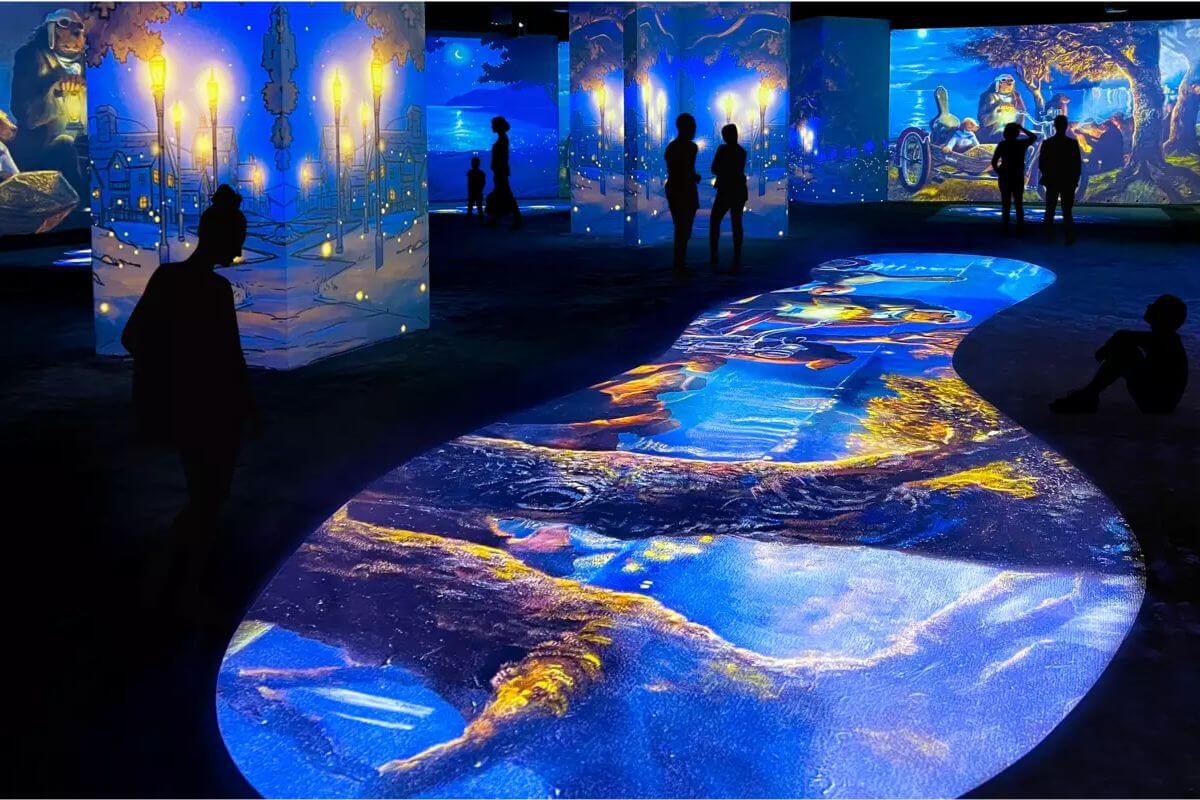 People standing in gallery with a variety of art projected on the walls and floors. 