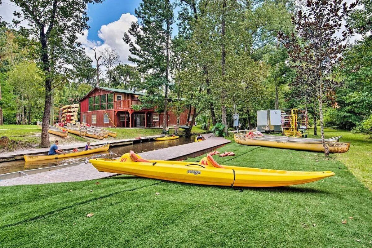 Kayaks on the ground with a canoe nearby in the water. 
