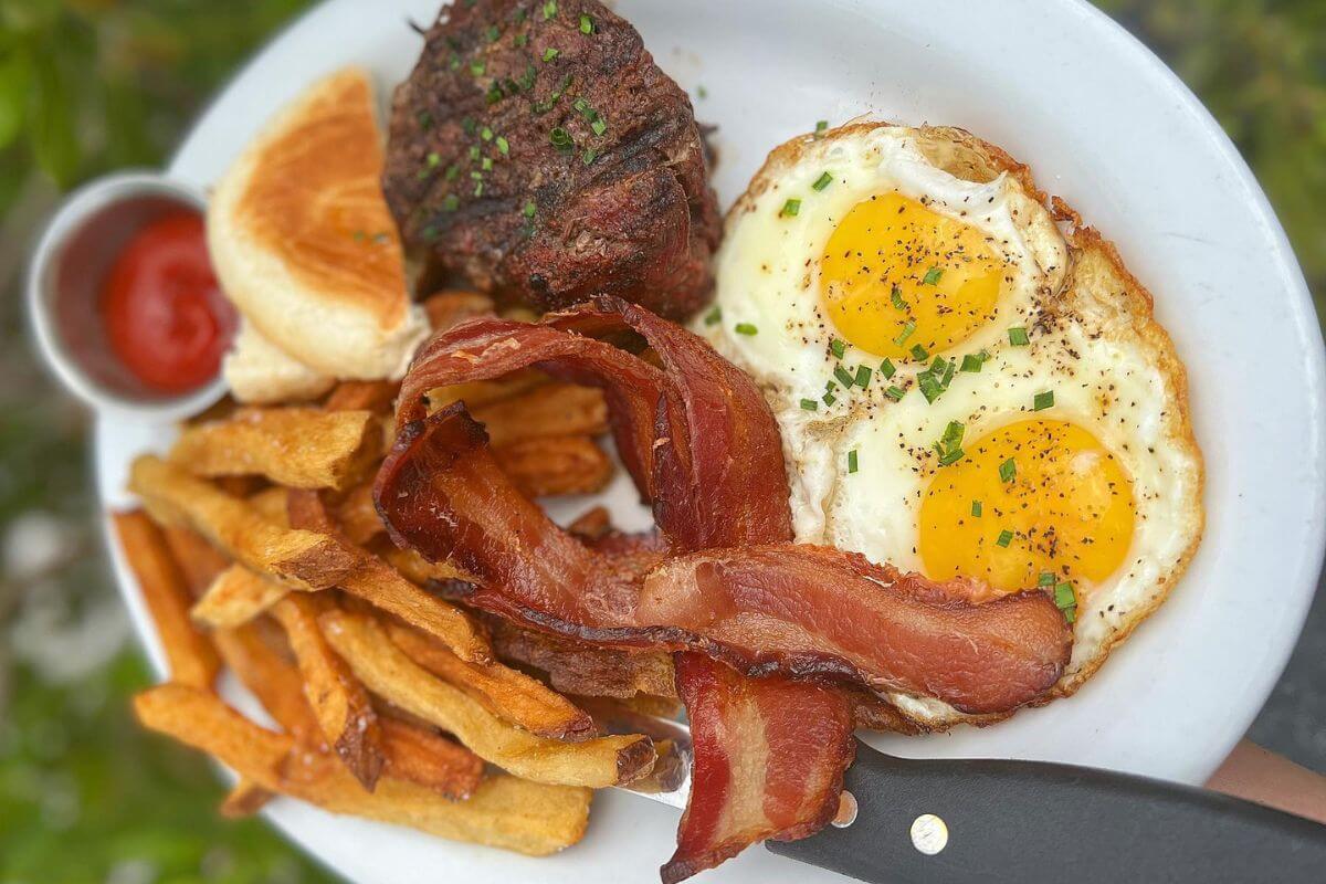 Eggs, steak, bacon, and fries on a plate. 