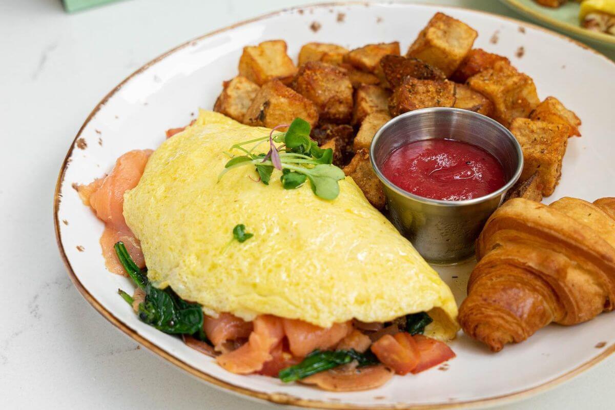 Omelet, potatoes, and a croissant on a plate. 