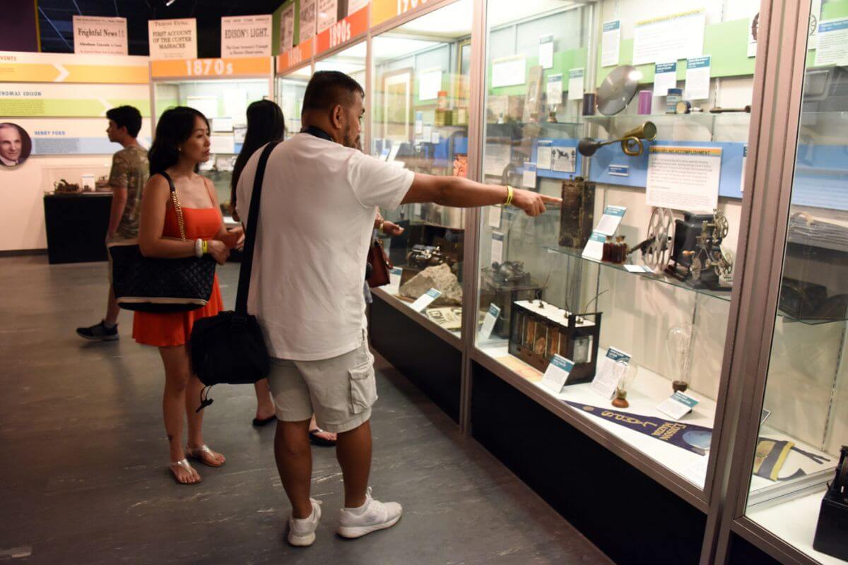 People looking at exhibit with musical instruments and other items on display. 