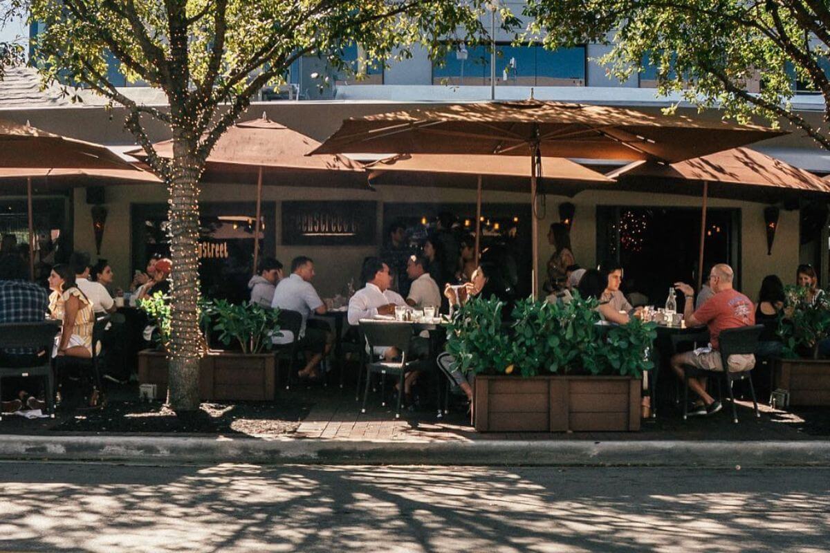 Outdoor view of a restaurant with guests sitting at tables under unbrellas. 