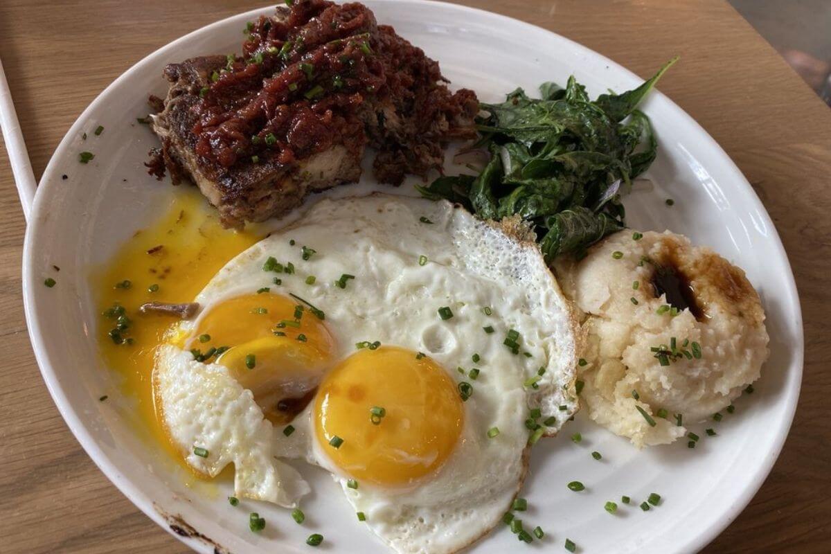 Plate with eggs, meat, spinach, and potatoes. 