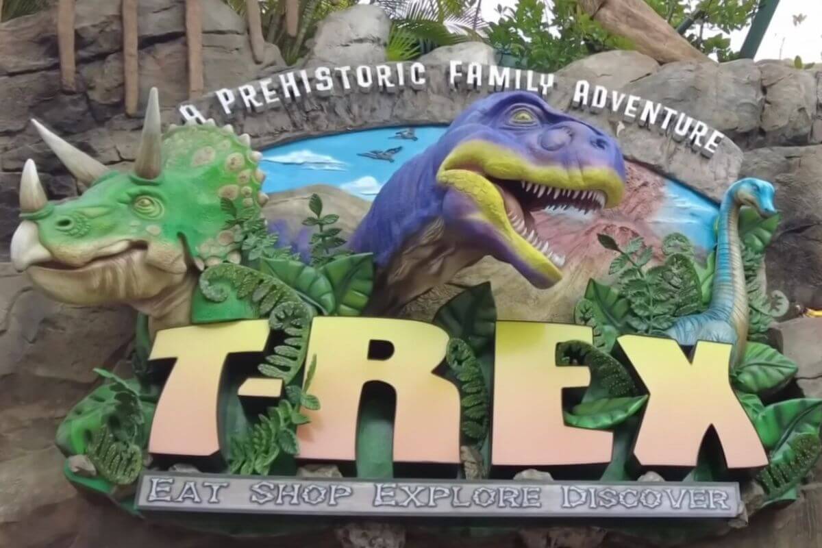 Sign with dinosaurs. Sign reads A Prehistoric Family Adventure T-Rex eat shop explore discover. 