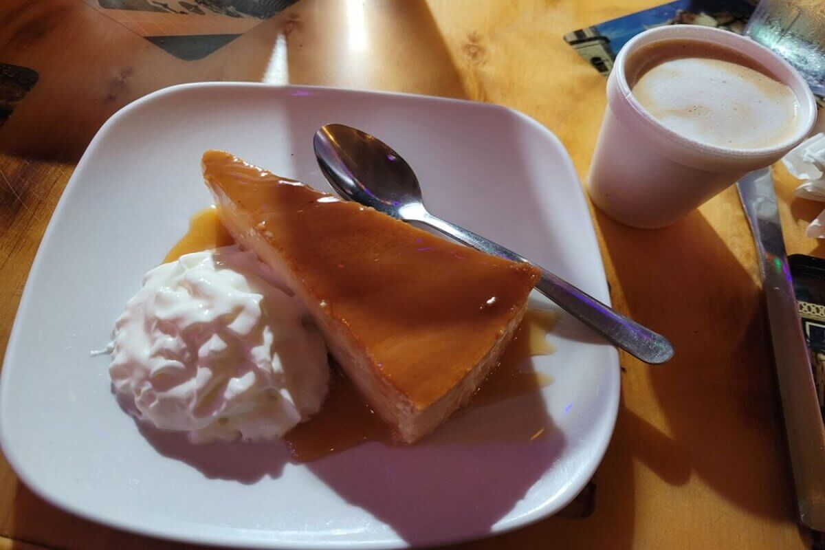 Flan and whipped cream on a plate with a cuban coffee in a cup next to it. 