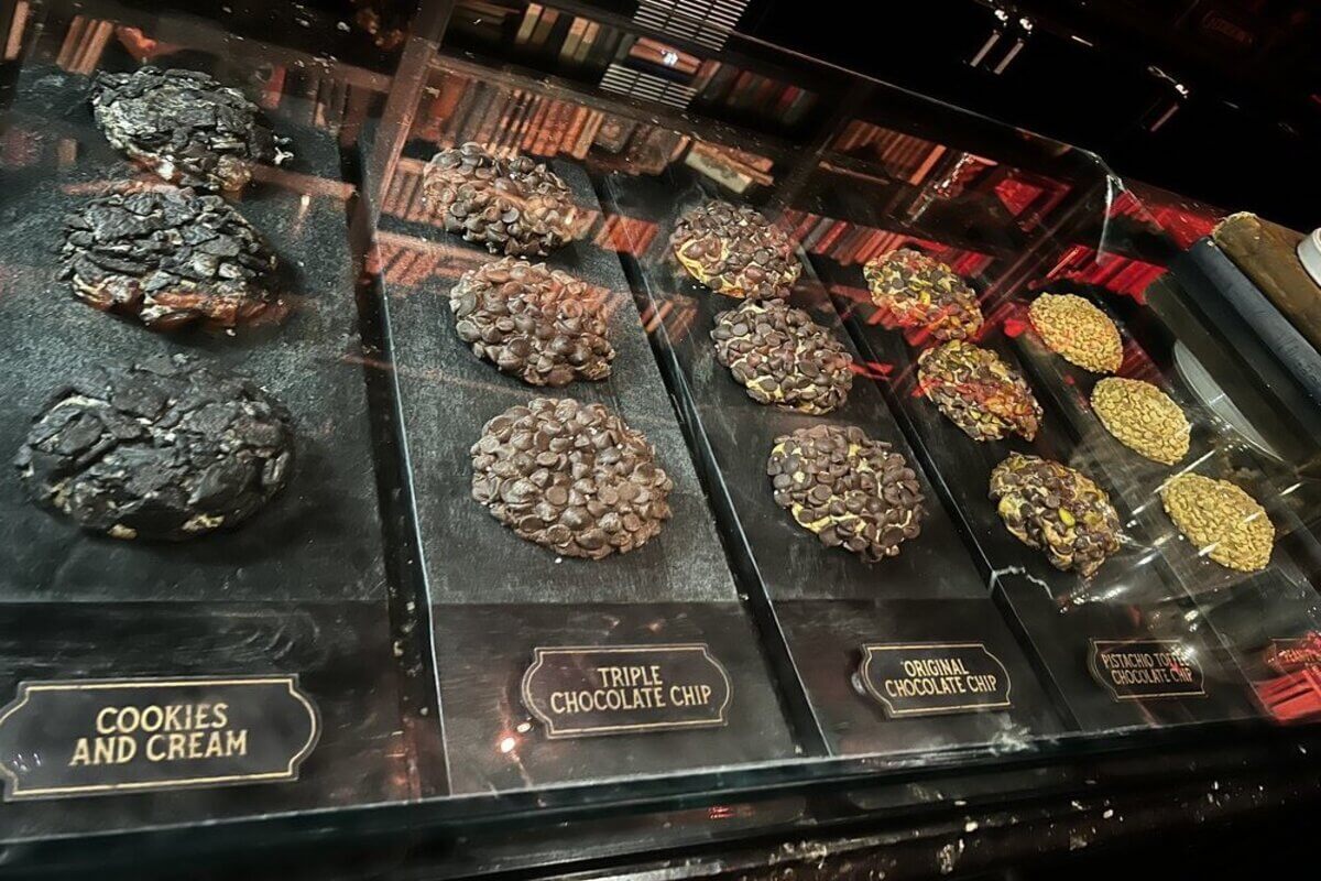 Selection of cookies in a display. Labels read Cookies and Cream, triple Chocolate chip, original chocolate chip, and pistachio toffee chocolate chip. 