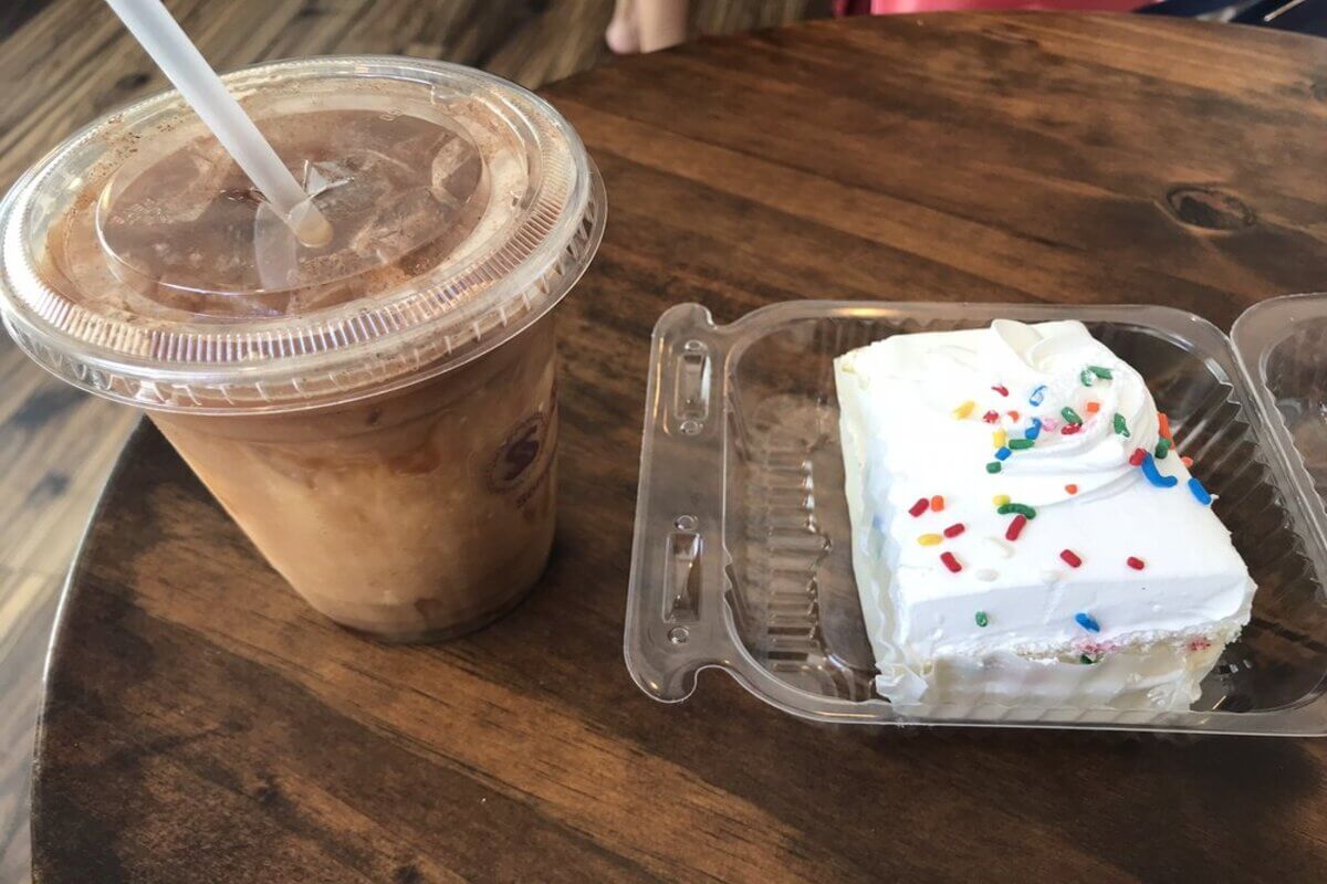Coffee in a cup and cake in a container on a table top. 