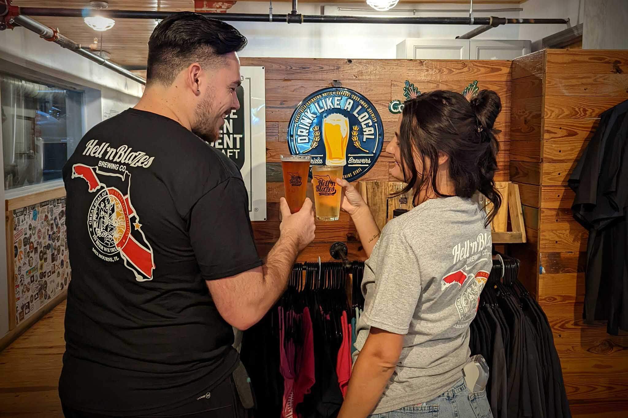 Two people holding glasses of beer at Hell ‘n Blaze Brewing. 