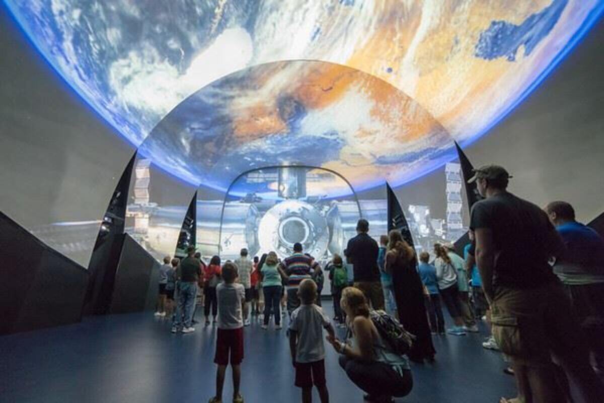 A group of people watching a screen with a planet depticted on it. 
