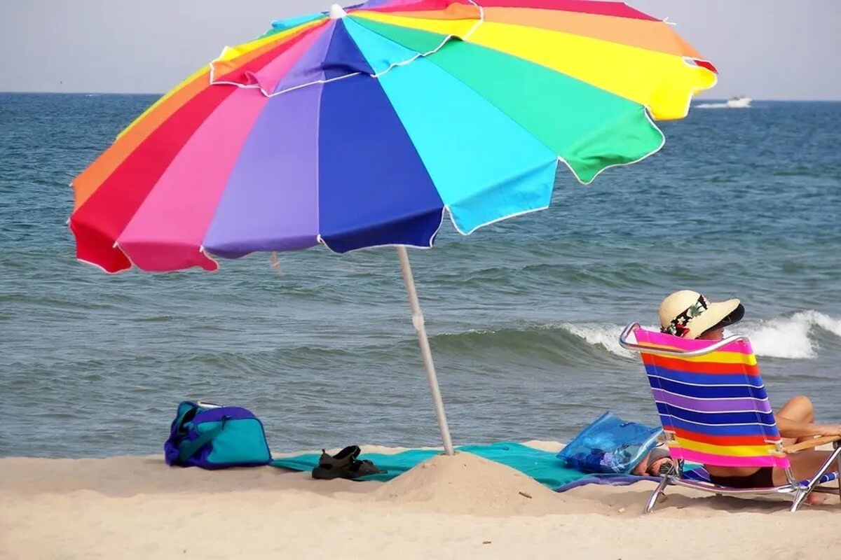 Person sitting in a beach chair under a beach umbrella. 