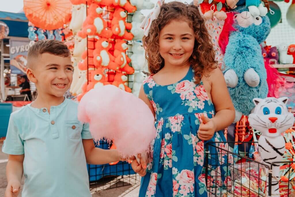 two children holding cotton candy with game prizes surrounding them