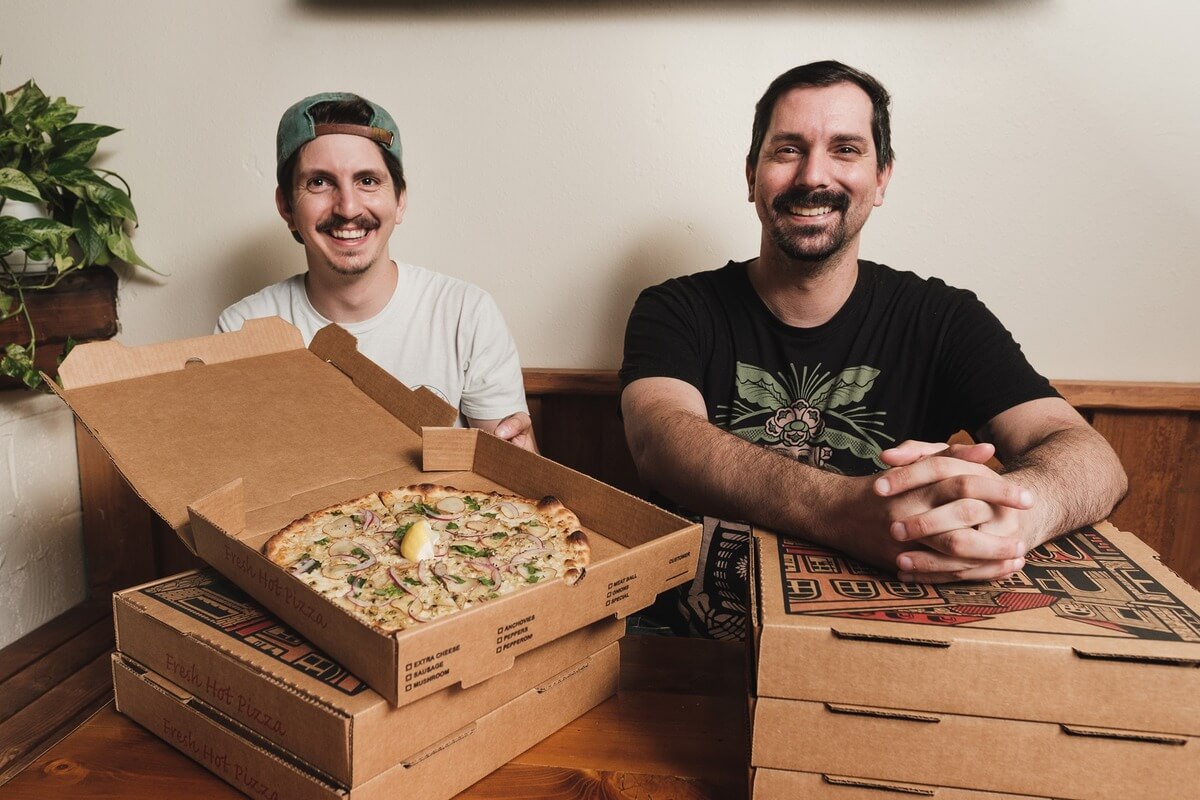 owners smiling next to pizza